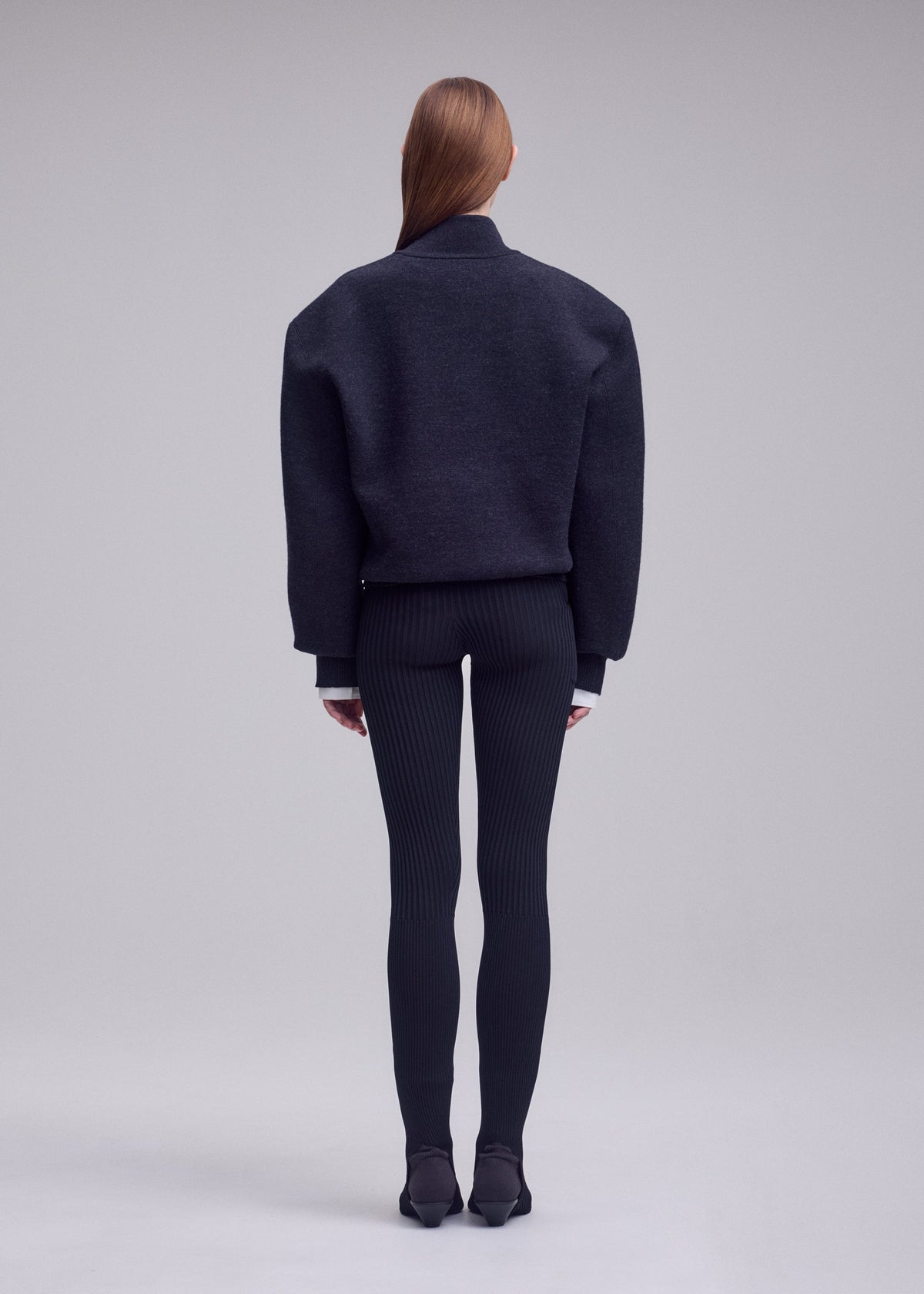A person with long straight hair, seen from behind, wears the HANDSOME KNIT by ISSEY MIYAKE, paired with ribbed black leggings and black shoes against a plain light gray background. view 5 of 6