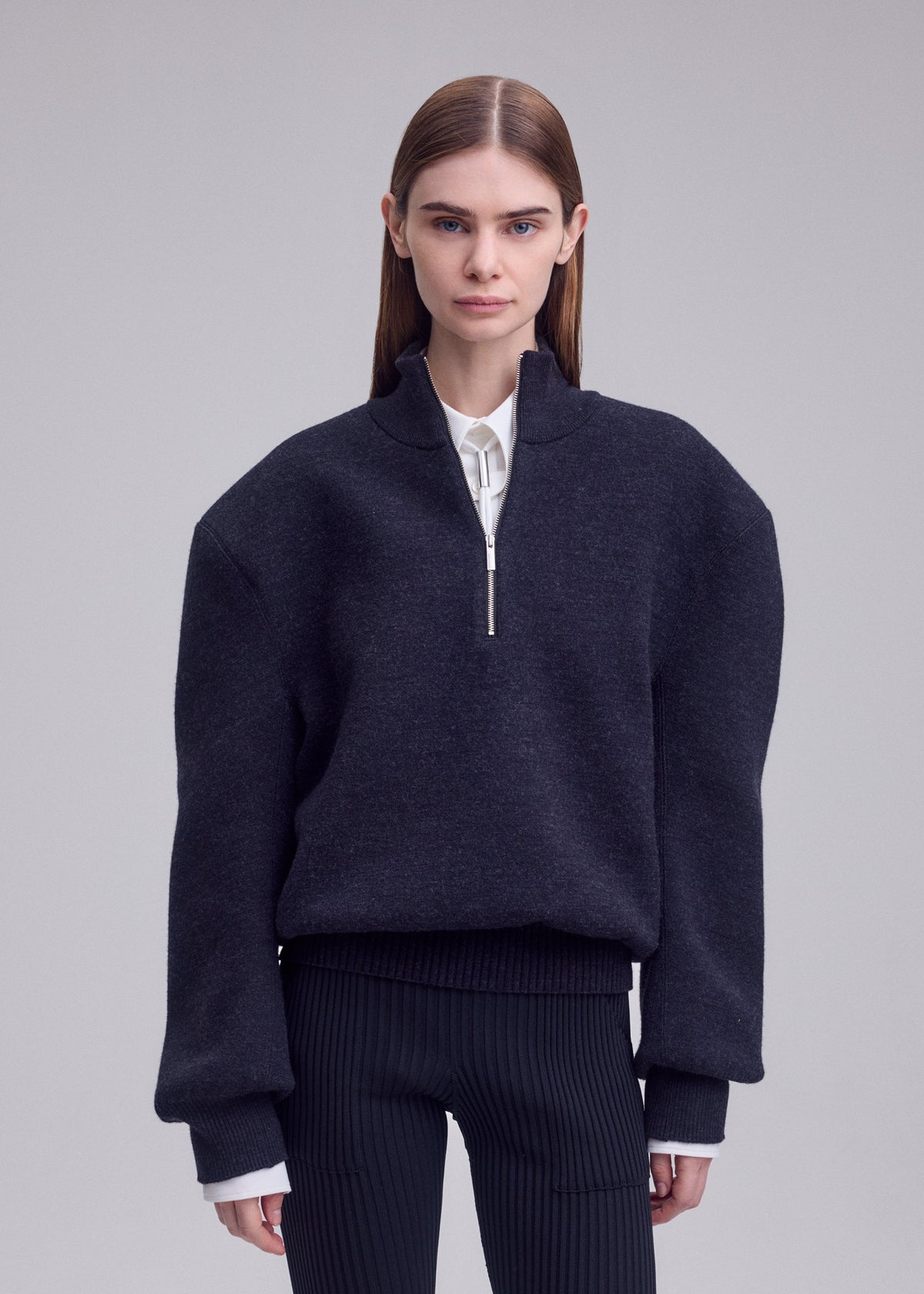 A person with straight brown hair wears a dark oversized ISSEY MIYAKE HANDSOME KNIT over a white shirt and black pinstriped pants, standing against a plain light gray background. view 6 of 6