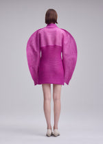 A person faces away, wearing a bright pink ISSEY MIYAKE PANINI PULLED dress with large rounded sleeves and a high collar. Cream shoes finish the look against a plain light background.