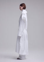 A person with short brown hair stands in profile wearing the ISSEY MIYAKE FOLDING COAT, featuring oversized sleeves and a high collar, set against a plain light gray background.