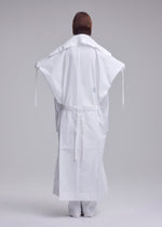 A person stands facing away in ISSEY MIYAKE's FOLDING COAT, featuring a minimalist, structured design with wide sleeves and a belt, set against a plain light gray background.