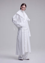 A person with short brown hair wears an ISSEY MIYAKE FOLDING COAT over white clothing and gray shoes, standing against a plain light gray background.