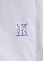 Close-up of white fabric from the ISSEY MIYAKE FOLDING COAT, featuring a blue, square-shaped stamp with ISSEY MIYAKE in stylized, abstract letters.