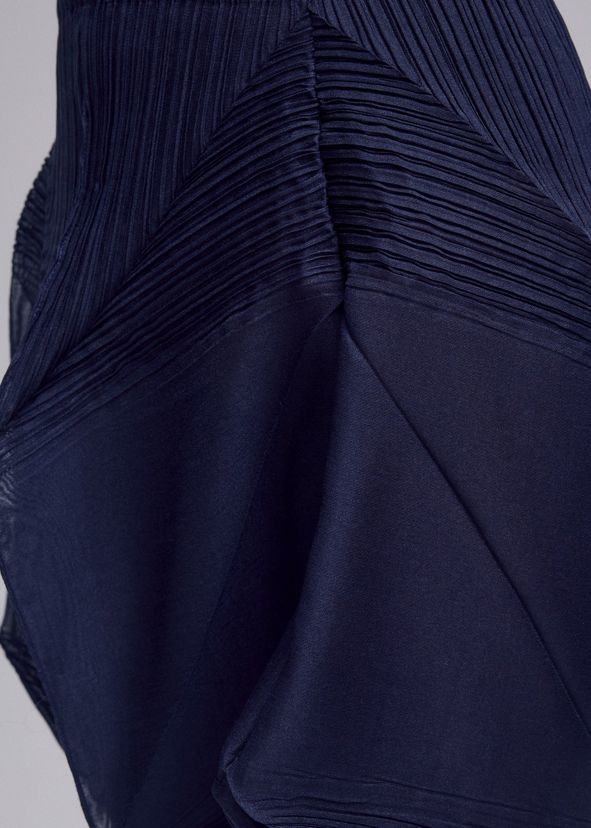 Close-up of the SHADE AND SHADED_NY skirt by ISSEY MIYAKE in dark blue, featuring pleated and smooth geometric sections. The slightly shiny fabric adds depth, highlighting the garment's unique architectural design. view 11 of 11
