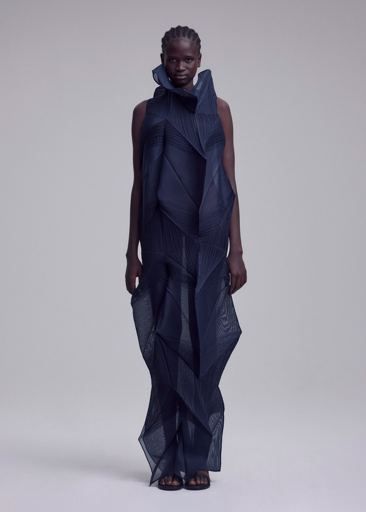 A model wears the SHADE AND SHADED_NY dress by ISSEY MIYAKE—a sleeveless, high-neck, dark blue geometric ankle-length dress crafted from sheer, layered fabric with bold angular patterns and a sculptural silhouette. view 3 of 10