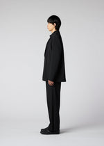 A person with straight black hair stands in profile against a plain light gray background, wearing the IM MEN WINGS loose-fitting black suit with wide pants and black shoes.