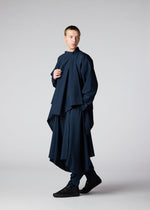 A person wears the IM MEN FLAT DRAPE set—loose, voluminous navy blue top with matching wide pants and black shoes—standing in a studio against a plain light background, looking to the side.
