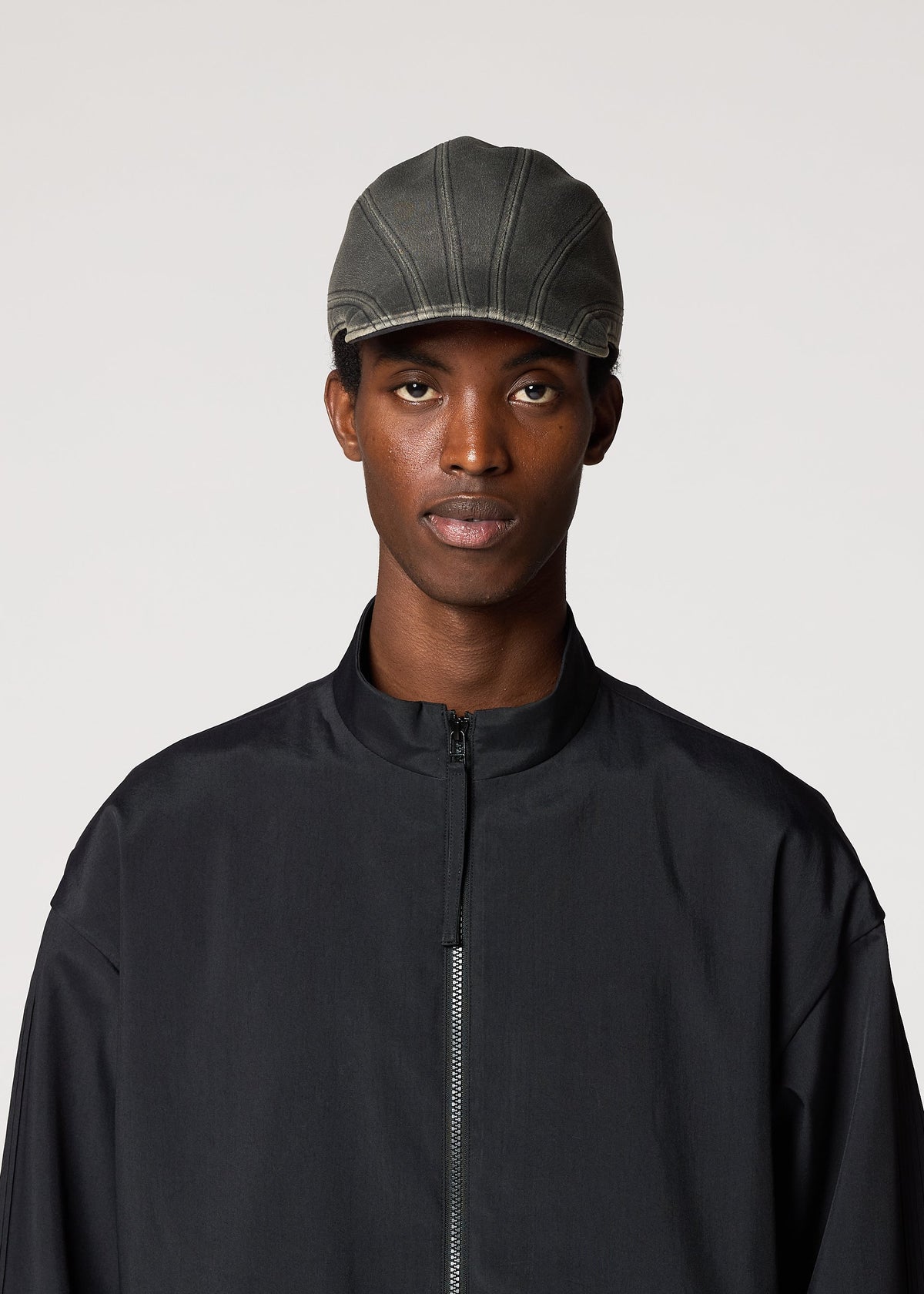 A person wearing the IM MEN CARVED CAP and a black zip-front jacket stands against a plain light background, looking directly at the camera with a neutral expression. view 4 of 6