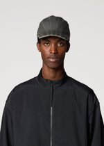 A person wearing the IM MEN CARVED CAP and a black zip-front jacket stands against a plain light background, looking directly at the camera with a neutral expression.