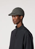 A person wearing the IM MEN CARVED CAP, a dark adjustable cap with a three-dimensional pattern, and a black zip-up jacket stands against a plain light background facing left.