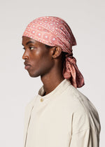 A person in profile wears the IM MEN UROKOMON STOLE, a pink patterned cotton accessory with a subtle scale-like design, paired with a light beige shirt against a plain light background.