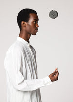 A person in a white button-down shirt stands in profile against a plain background, looking at the GURU GURU foldable tote bag from IM MEN as it levitates above their hand.