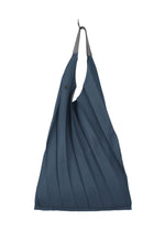 The GURU GURU tote by IM MEN is a dark blue, foldable bag featuring handmade pleats, a black button closure, gray top handles, and fits in your palm. It’s shown hanging on a hook against a white background. - DARK BLUE (no.73)