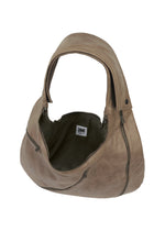 The CARVED LEATHER BAG by IM MEN is a spacious taupe natural leather bag with a wide handle, curved design, partially open zipper showing fabric lining and an inside white HMM label, plus an adjustable shoulder strap for versatile use.