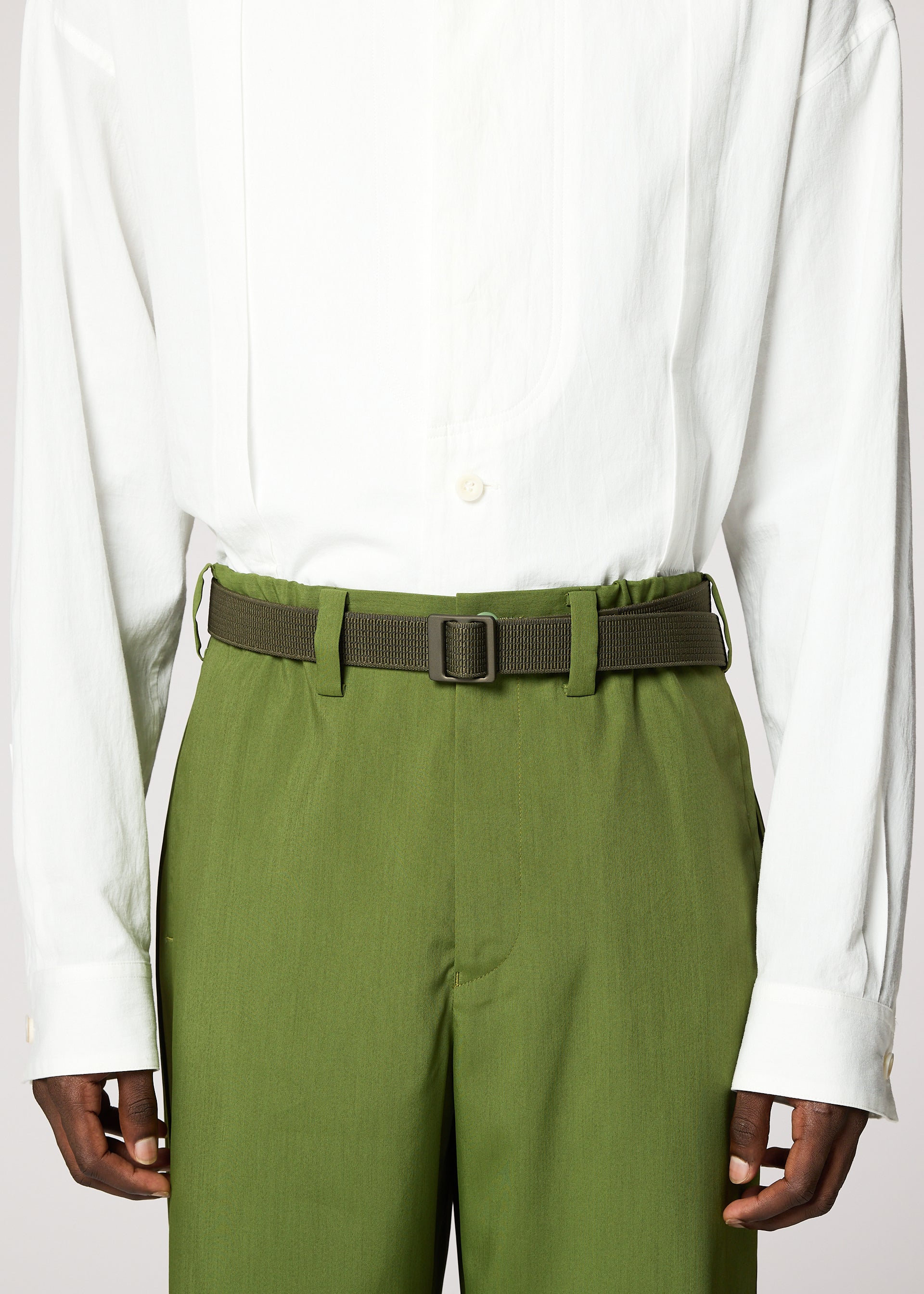Zoomed view A person wears a white button-down shirt tucked into high-waisted green trousers, styled with the IM MEN FRICTION BELT in matching green, shown from shoulders to upper thighs.