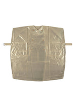 The GINTO FLAT by IM MEN is a flat, transparent beige straitjacket with buckles, straps, double-breasted buttons, and large front pockets, inspired by Shoji Kamoda. Displayed against a white background.