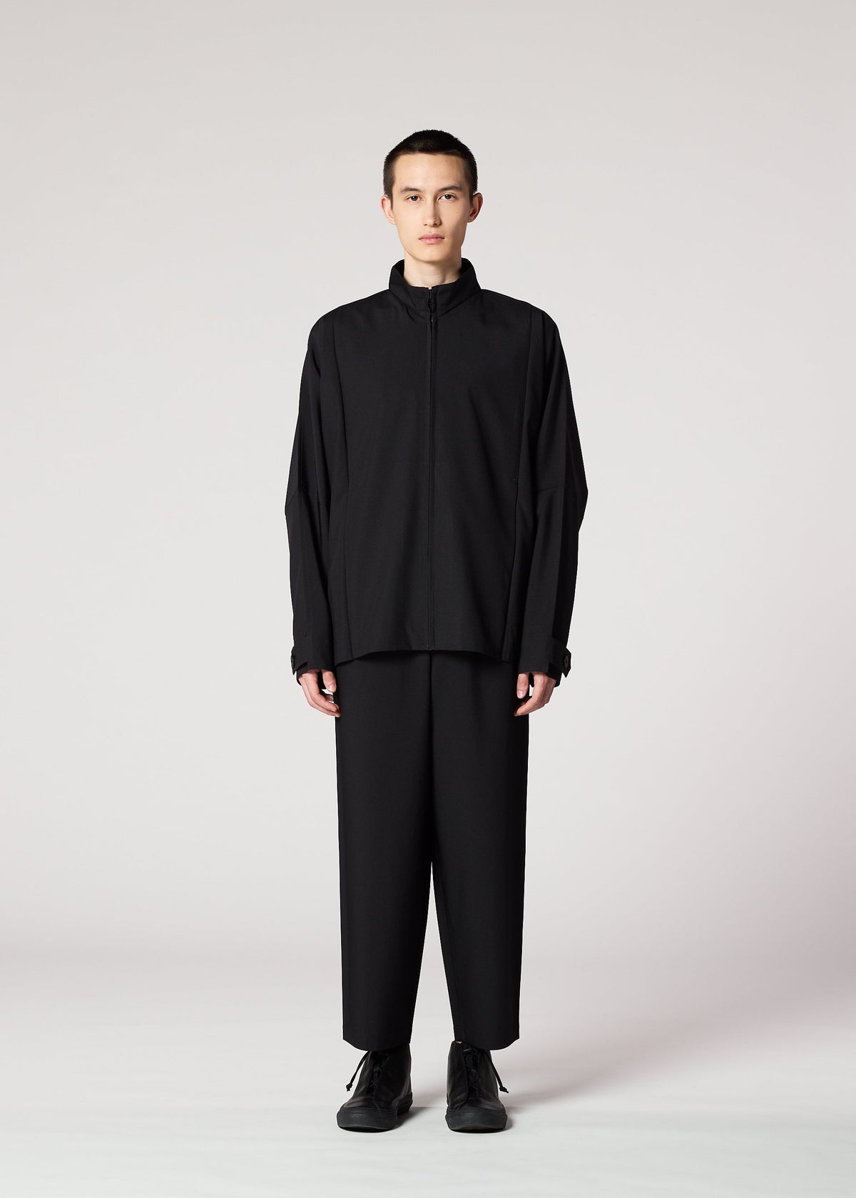 A person stands facing forward against a plain light background, wearing IM MEN’s FLAT BLACK wrinkle-resistant jacket and wide black pants, paired with black shoes. view 10 of 14