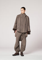 A person wears the IM MEN ENGRAVE set: a Shoji Kamoda-inspired jacquard loom jacket and wide balloon pants in taupe. The textured fabric has stitched, curved lines for a wave effect. Dark shoes complete the outfit.