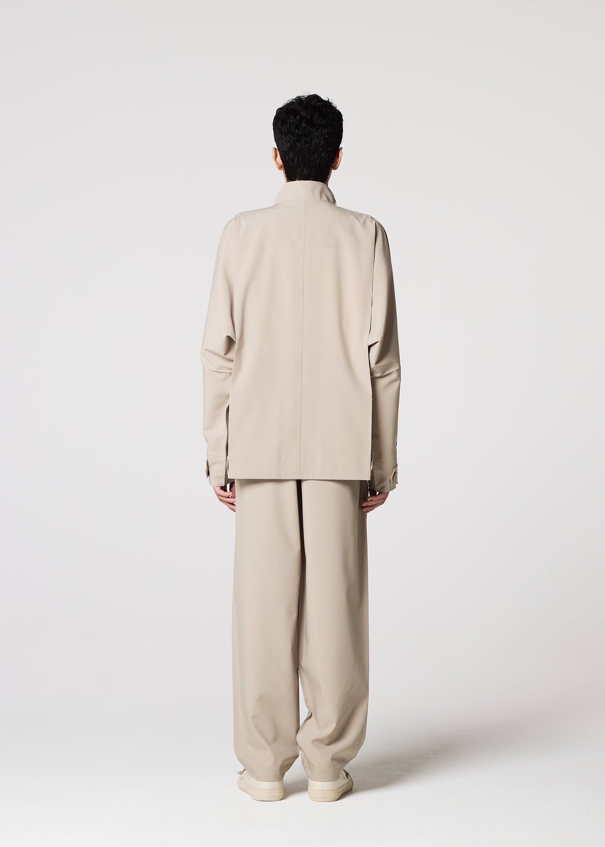 A person faces away from the camera, wearing the IM MEN FLAT wrinkle-resistant light beige jacket with wide-leg pants and matching shoes, set against a plain light background. view 12 of 13