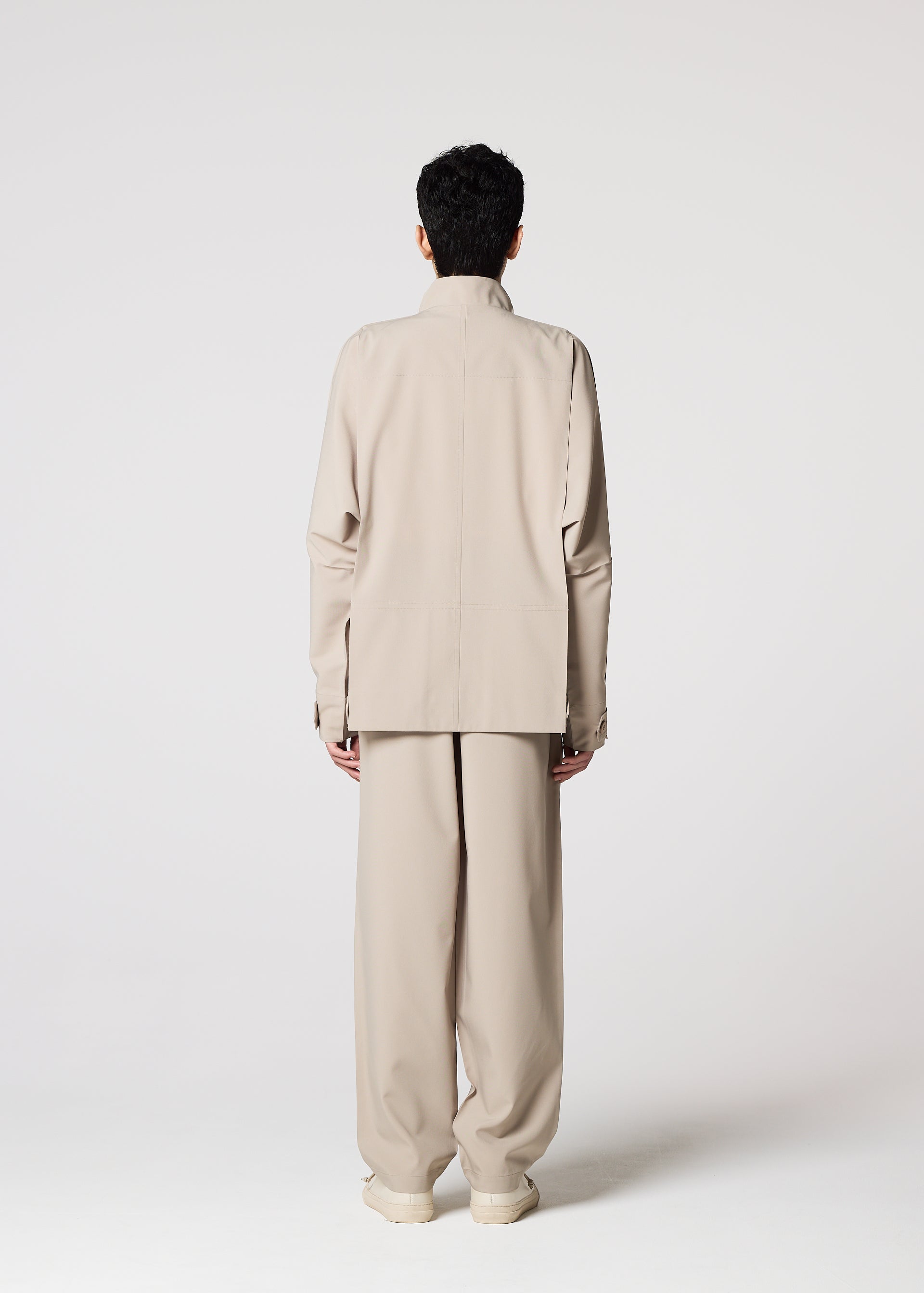 Zoomed view A person faces away from the camera, wearing the IM MEN FLAT wrinkle-resistant light beige jacket with wide-leg pants and matching shoes, set against a plain light background.
