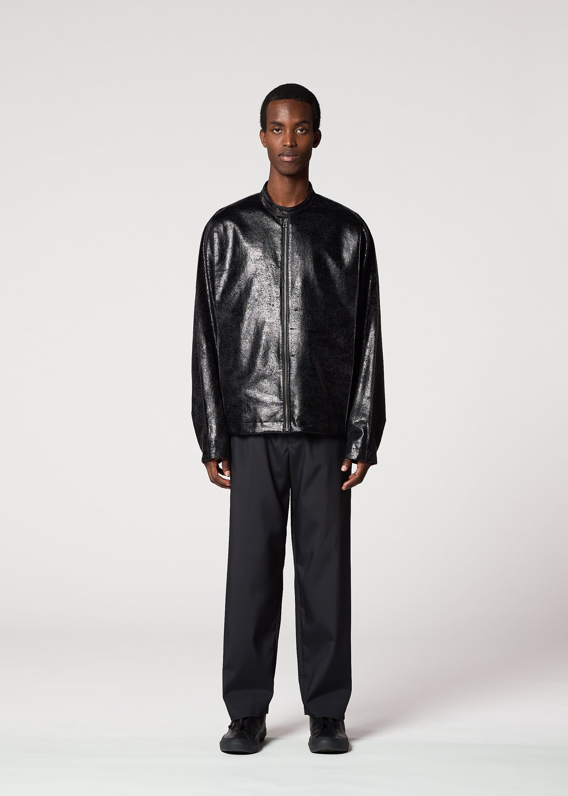 Zoomed view A man stands facing forward against a plain light background, wearing the GINTO silver foil jacket by IM MEN, paired with black trousers and black shoes. His hands rest by his sides, and his expression is neutral.