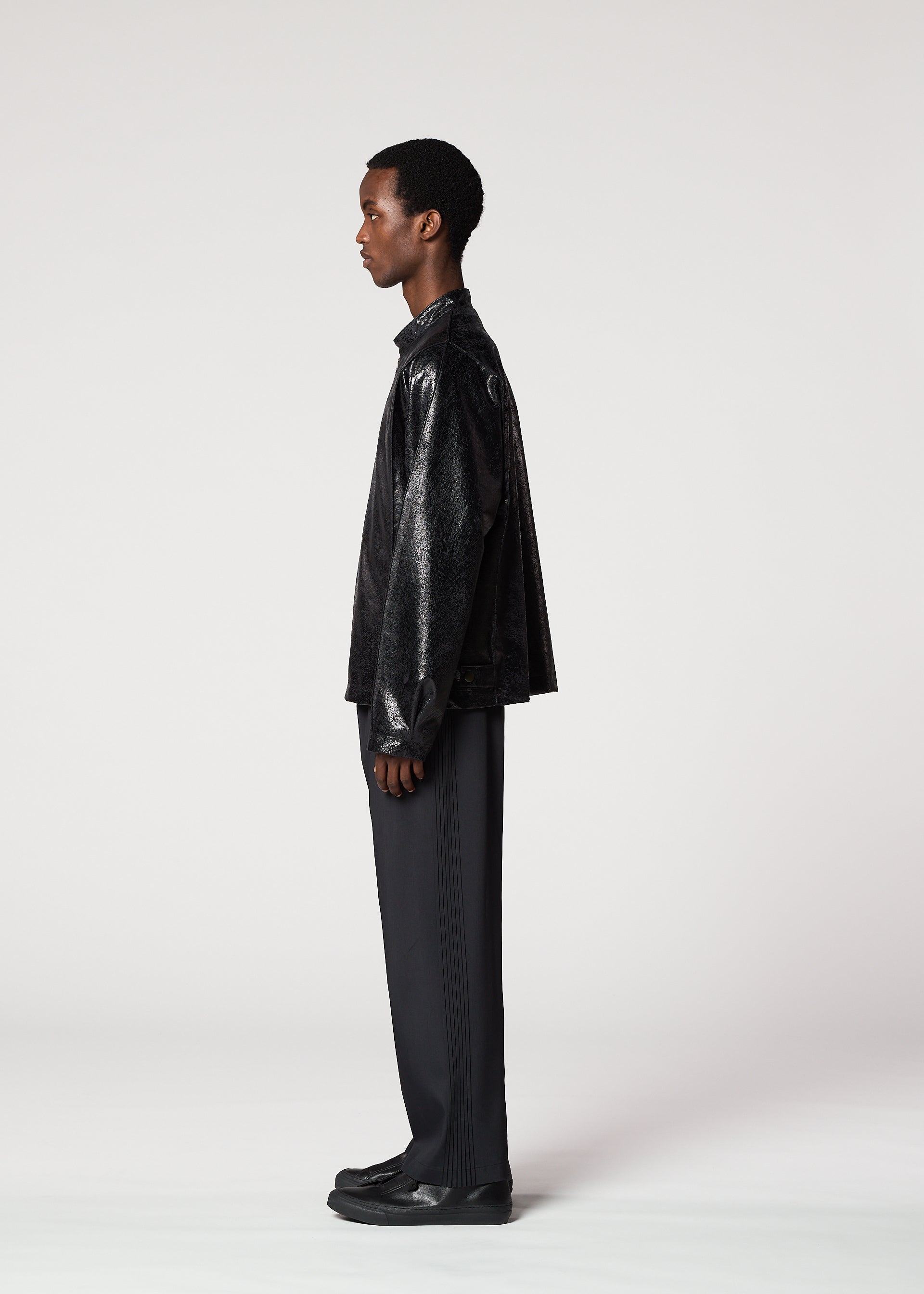 Zoomed view A person in profile against a plain background, wearing the IM MEN GINTO black plant-derived artificial suede leather-textured jacket, paired with dark pleated pants and black shoes.