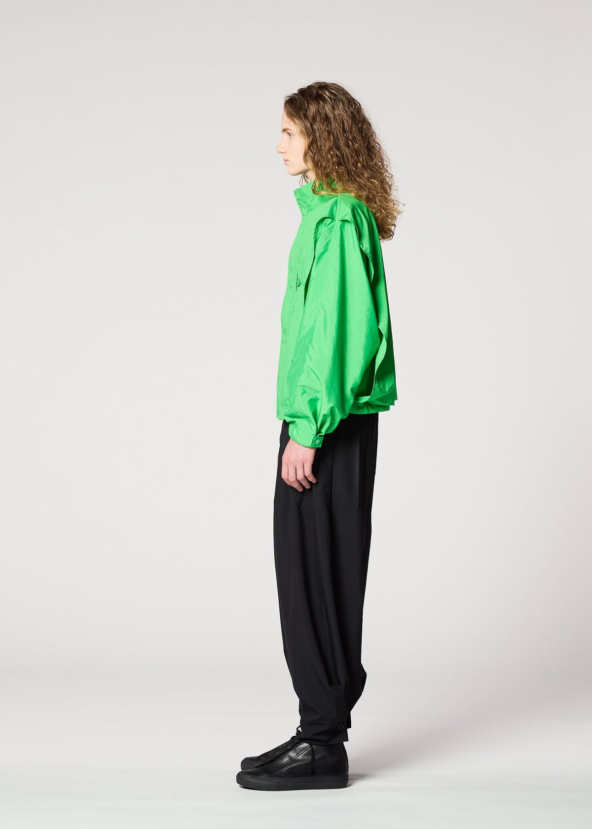 Wearing IM MEN’s FISHING NET NYLON jacket—bright green, lightweight, and made from recycled fishing nets—a person with curly hair stands in profile against a plain background, paired with loose black pants and black shoes. view 7 of 9