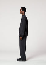 A man stands in profile against a plain white background, dressed in IM MEN's AIR PLEATS lightweight, wrinkle-resistant black jacket and matching pants, paired with black shoes.