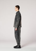 A person stands in profile against a plain light background, wearing IM MEN’s ELEMENTS set: a matching faded black denim jacket and pants with black shoes, featuring color-fading inspired by ceramic artist Shoji Kamoda’s signature style.