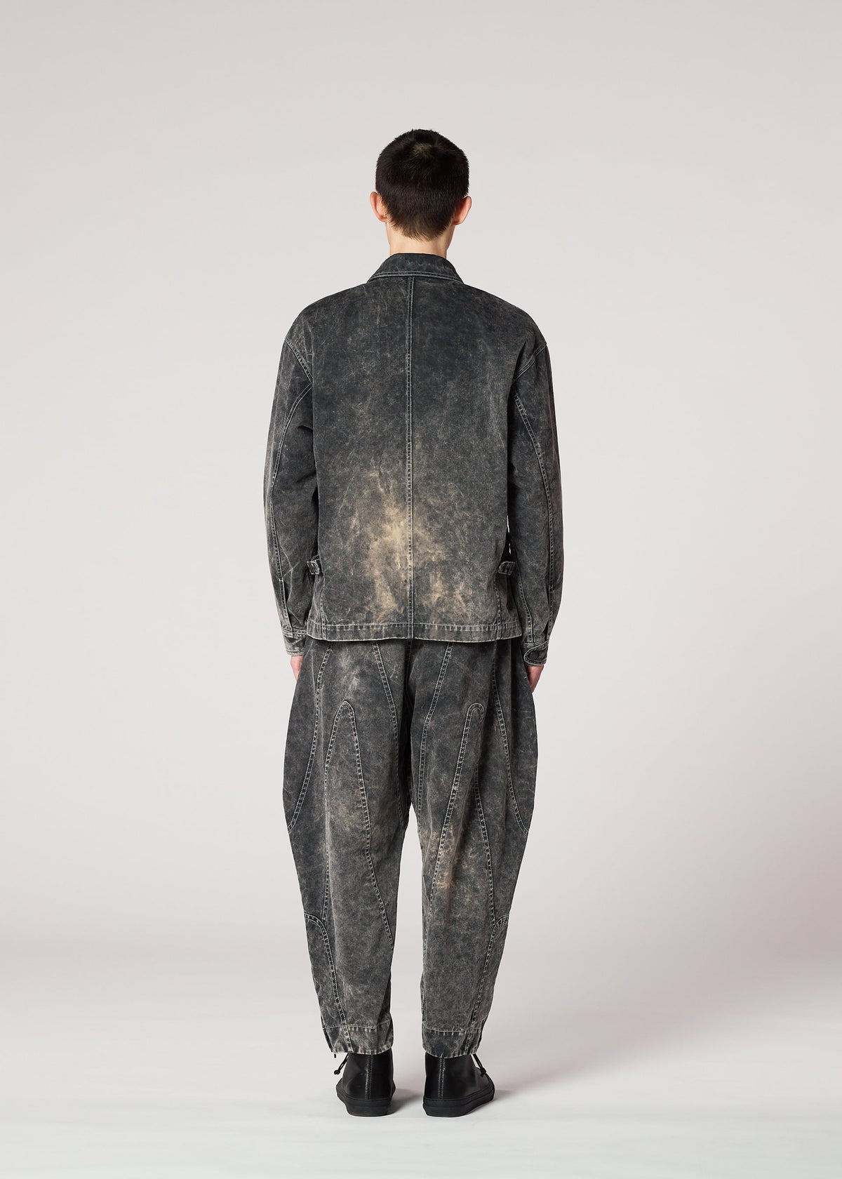 A person faces away, wearing IM MEN's ELEMENTS loose black denim jacket with color-fading and matching baggy pants. The casual, slightly distressed outfit is set against a plain light background. view 7 of 8