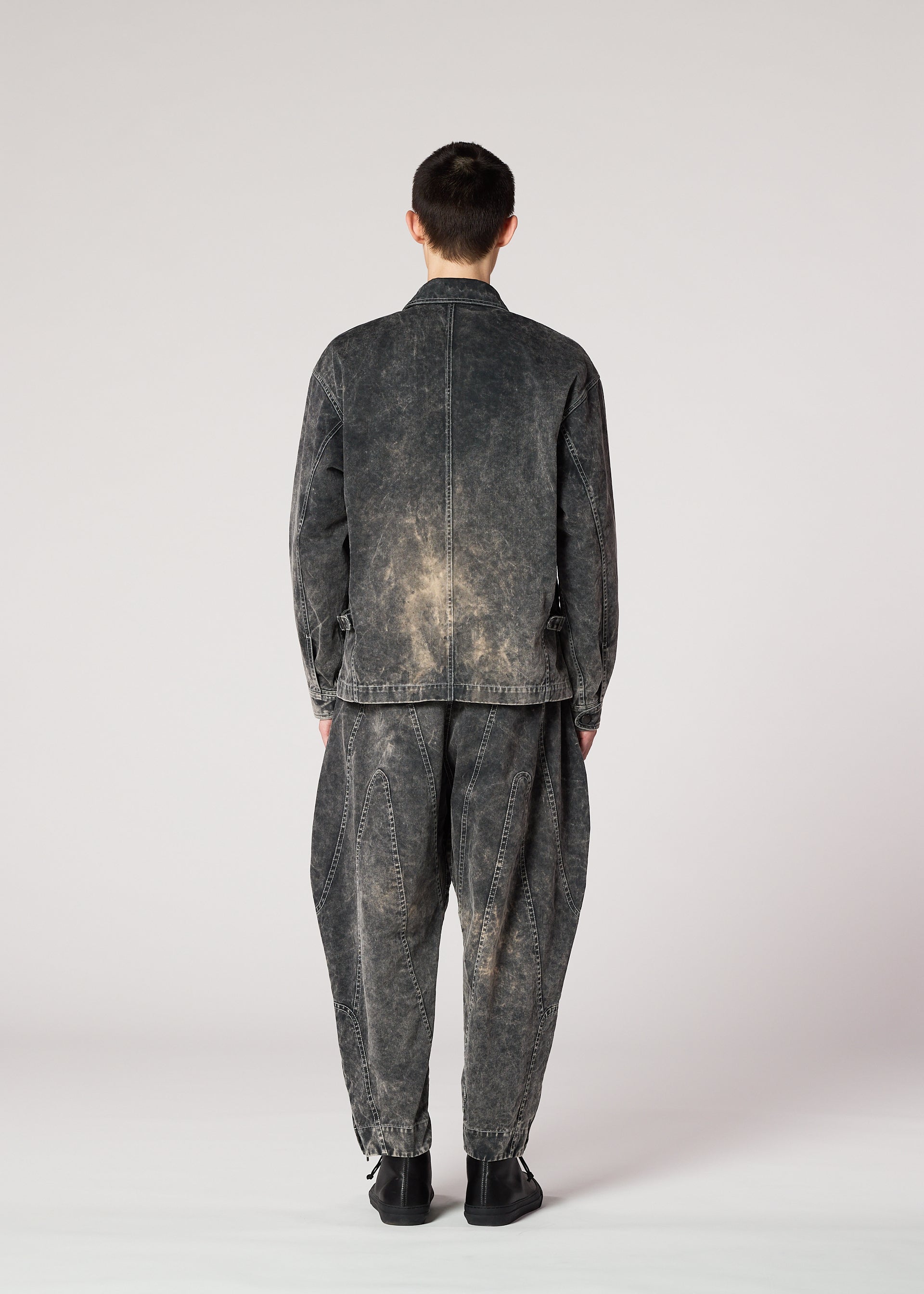 Zoomed view A person faces away, wearing IM MEN's ELEMENTS loose black denim jacket with color-fading and matching baggy pants. The casual, slightly distressed outfit is set against a plain light background.