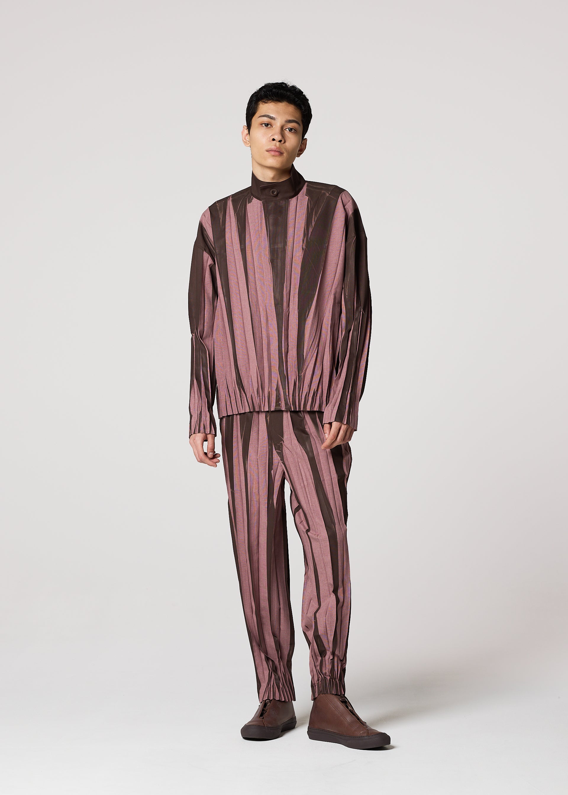 Zoomed view A person stands against a plain light background wearing the IM MEN EDGE matching set—loose, long-sleeved top and pants with vertical maroon and brown abstract stripes—paired with brown shoes.