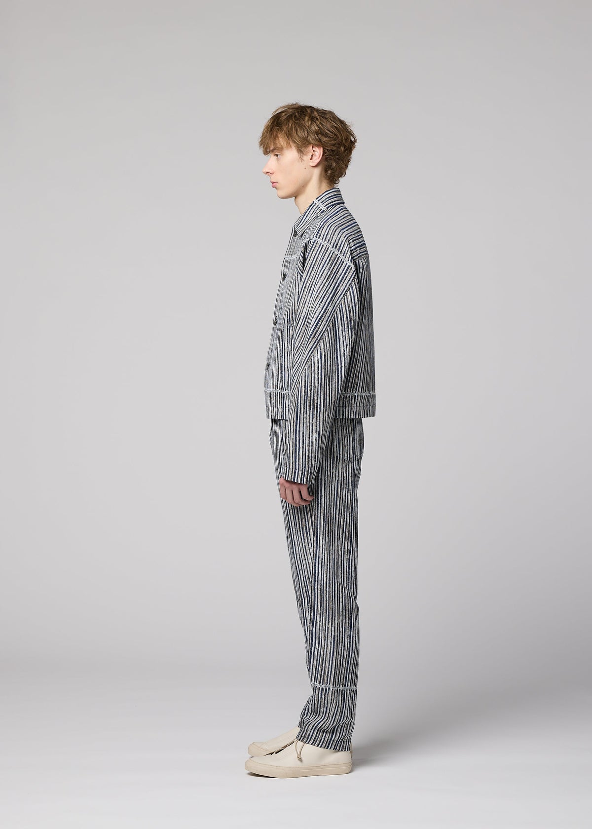 A person with short light brown hair stands in profile against a light gray background, wearing the IM MEN CURVINESS cotton-linen textured jacket and matching striped pants set, paired with light-colored shoes. view 6 of 8