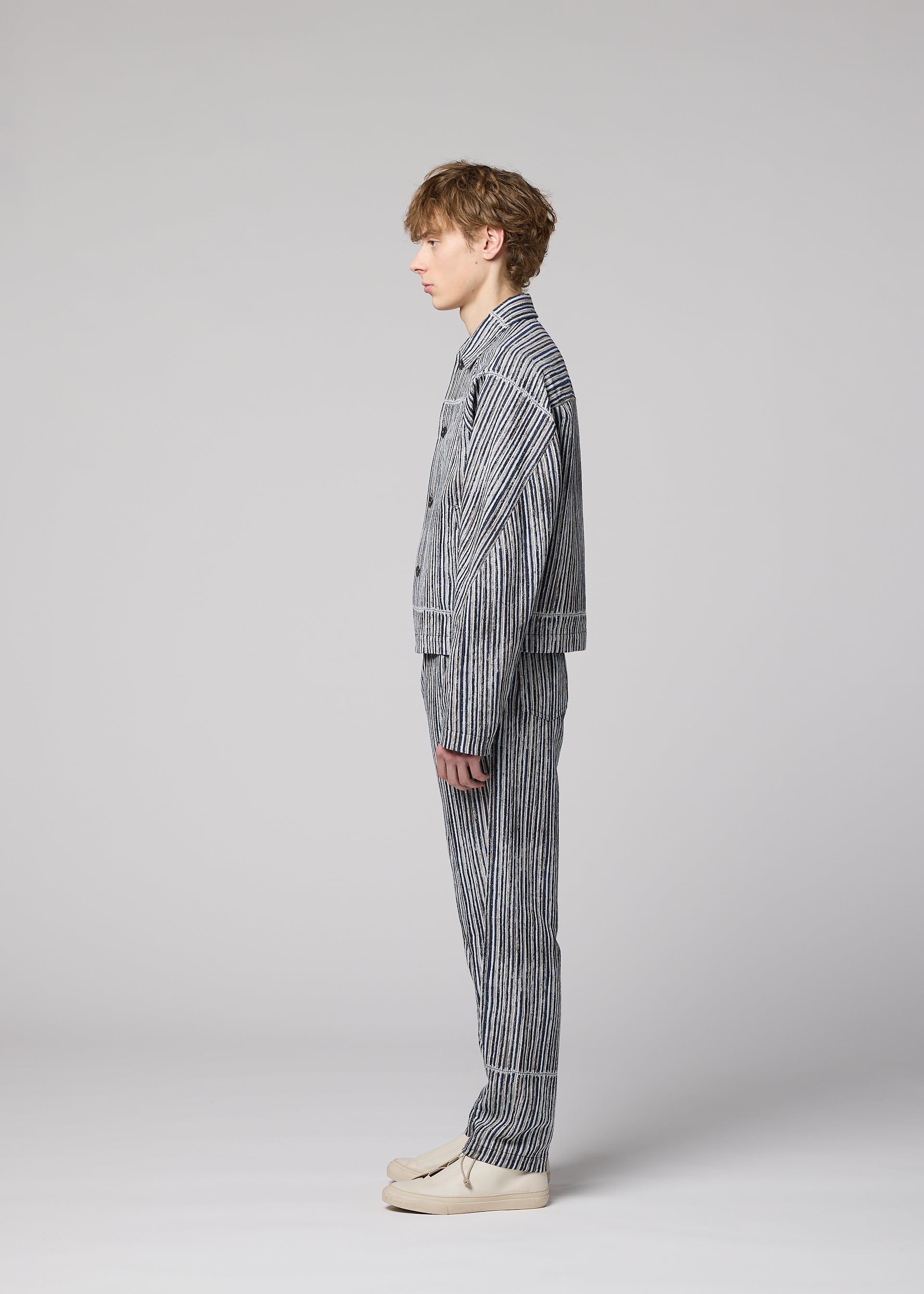 Zoomed view A person with short light brown hair stands in profile against a light gray background, wearing the IM MEN CURVINESS cotton-linen textured jacket and matching striped pants set, paired with light-colored shoes.
