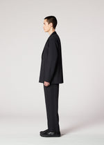 A person with short dark hair wears IM MEN's AIR PLEATS BLACK suit and black shoes, standing sideways facing left against a plain light gray background.