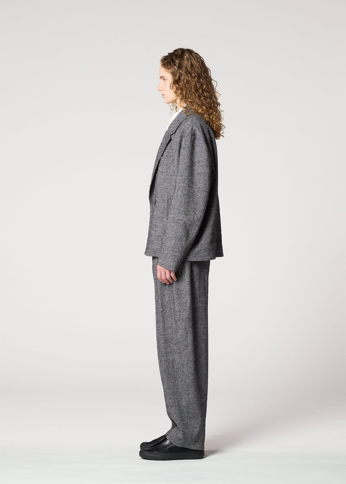 A person with curly hair stands in profile against a white background, wearing the IM MEN TEXTURES loose-fitting gray double-breasted jacket and black shoes. view 6 of 8