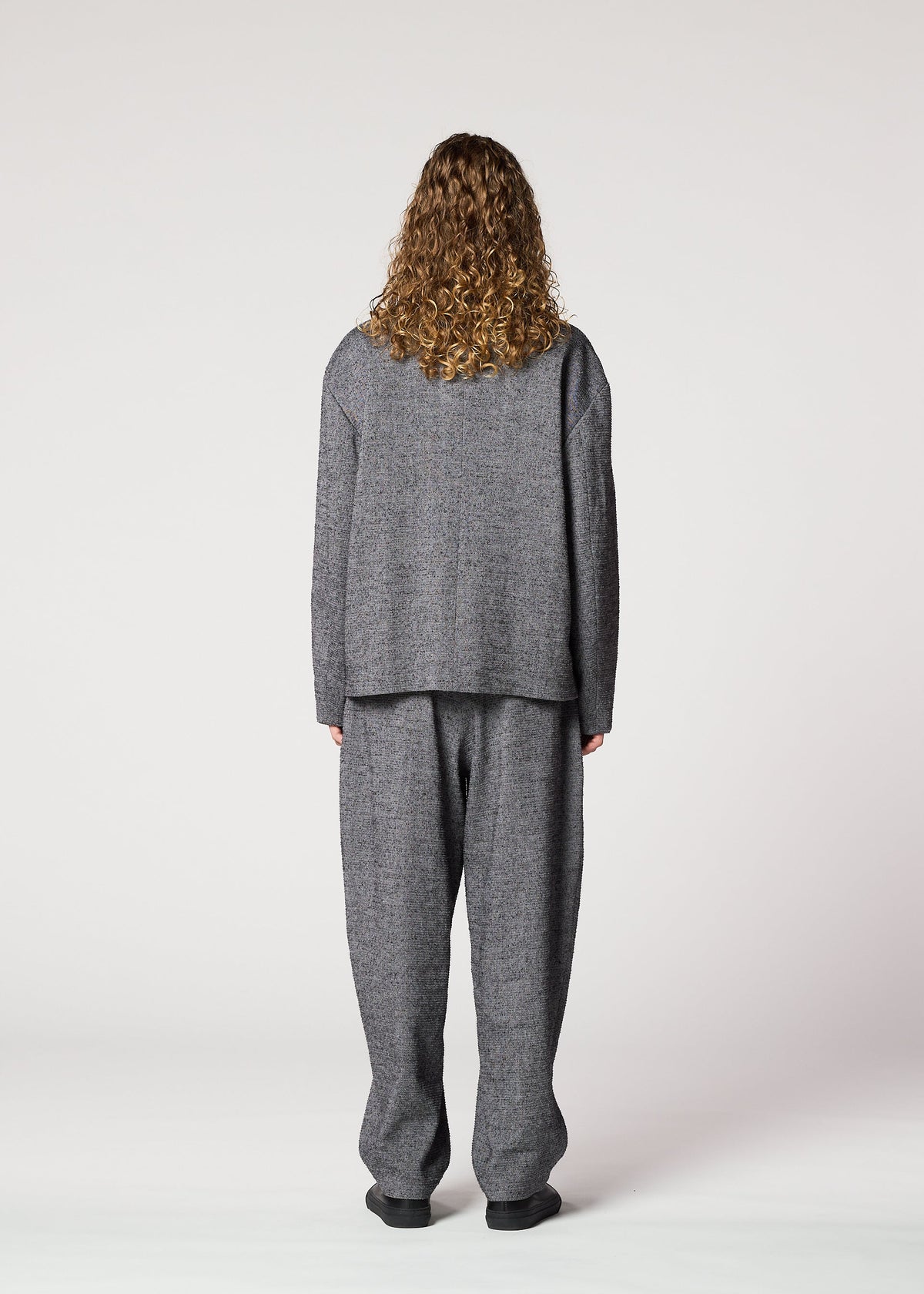 A person with curly hair is seen from behind wearing the IM MEN TEXTURES loose-fitting gray double-breasted jacket and wide pants suit, standing against a plain light background. view 7 of 8