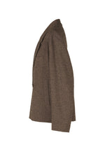 The IM MEN TEXTURES brown tweed blazer, inspired by ceramic textile artistry, is shown in a side view on a white background, highlighting its classic collar, lapel, chest pocket, and two side pockets.