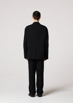 A man stands confidently in his black suit, wearing IM MEN’s SHRINK JACQUARD jacket featuring a subtle wood-grain woven pattern.