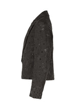 The UROKOMON short jacket by IM MEN features a black, textured scale-like design inspired by Shoji Kamoda, with a circular discs-and-rings pattern, shown from the side against a white background.