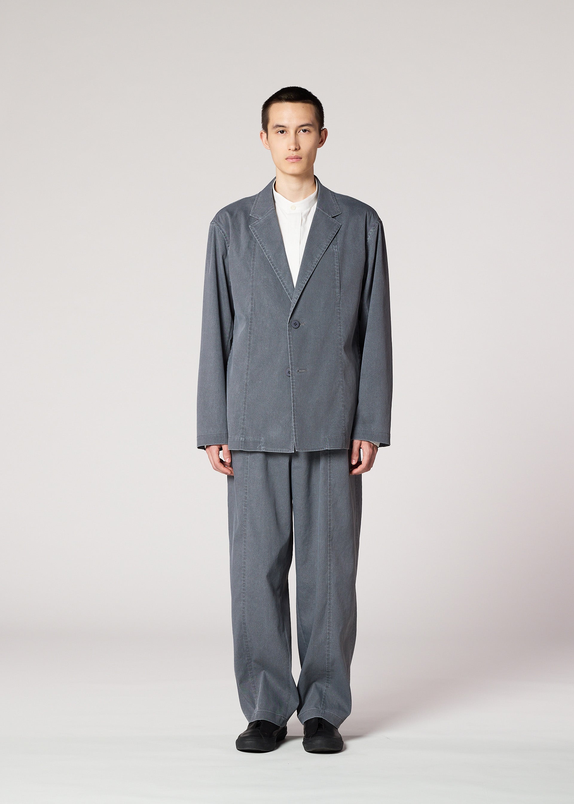 Zoomed view A person stands facing forward against a plain background, wearing the IM MEN AIR WASH gray plant-derived polyester suit jacket and matching wide-leg pants over a white shirt with black shoes.