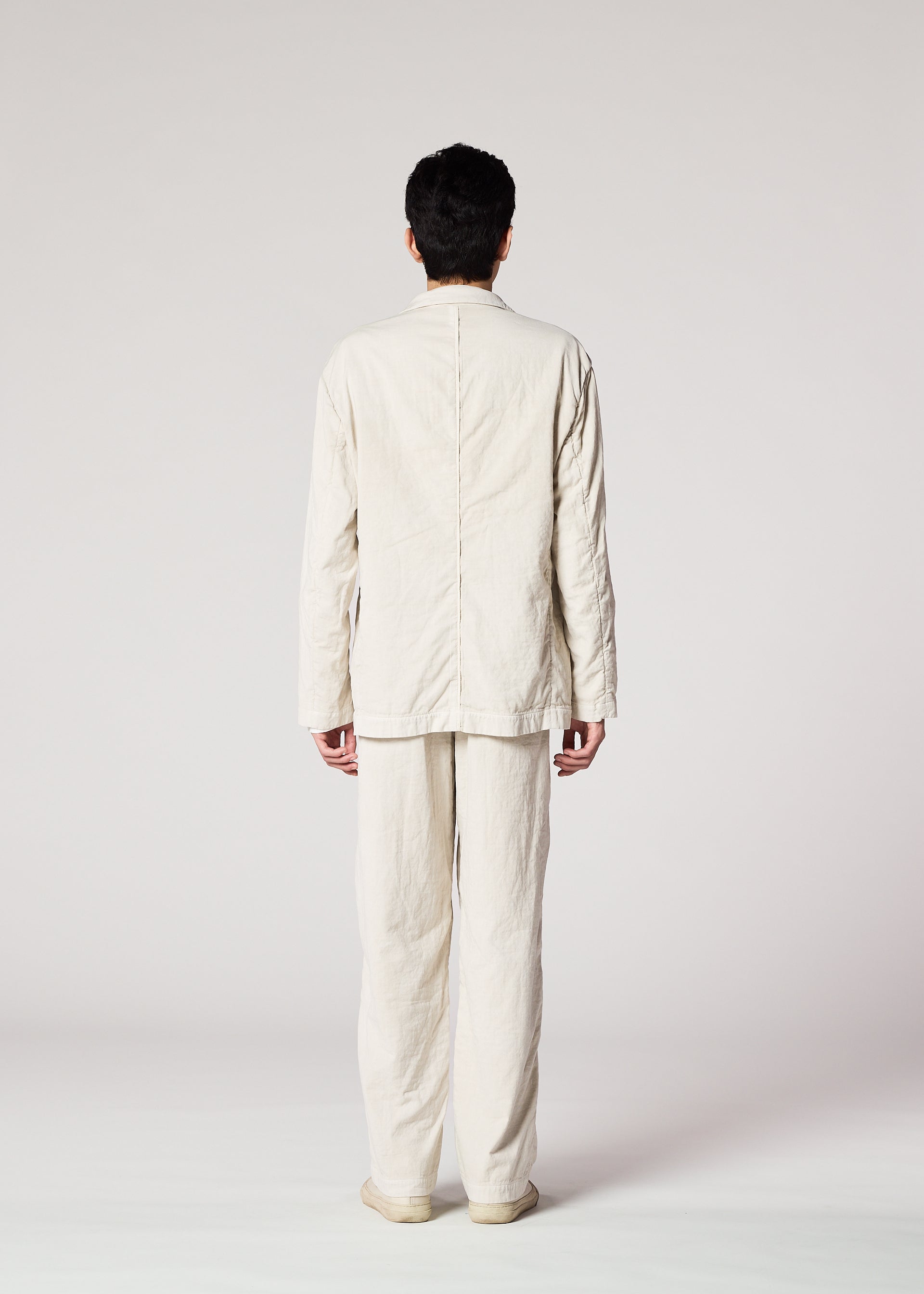 Zoomed view A person stands with their back to the camera, wearing IM MEN's PIGMENT DOUBLE FACE COTTON loose-fit light beige long-sleeve shirt and matching pants, arms relaxed by their sides, set against a plain light background.