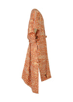 The IM MEN UROKOMON is a long, orange kimono-style robe with wide sleeves and geometric white circular, scale-like patterns, displayed on a mannequin from the side against a white background.
