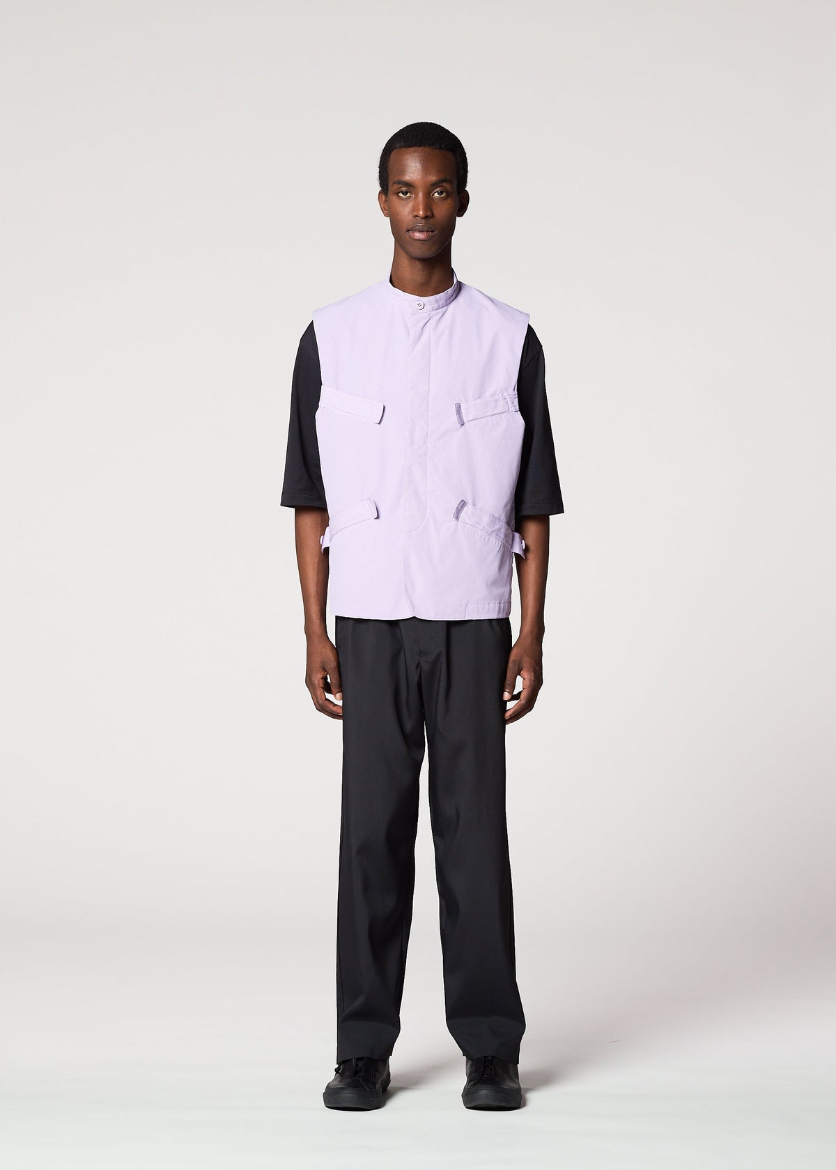 A person faces forward against a plain light background, sporting the IM MEN RESILIENCE lightweight lavender utility vest over a black short-sleeve shirt, paired with black pants and shoes for an everyday wear look. view 6 of 9