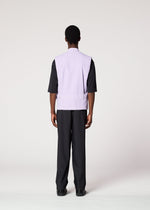 A person faces away from the camera, wearing IM MEN’s RESILIENCE—an airy light purple vest over a black elbow-sleeve shirt and black pants—ideal for everyday style, set against a plain light background.