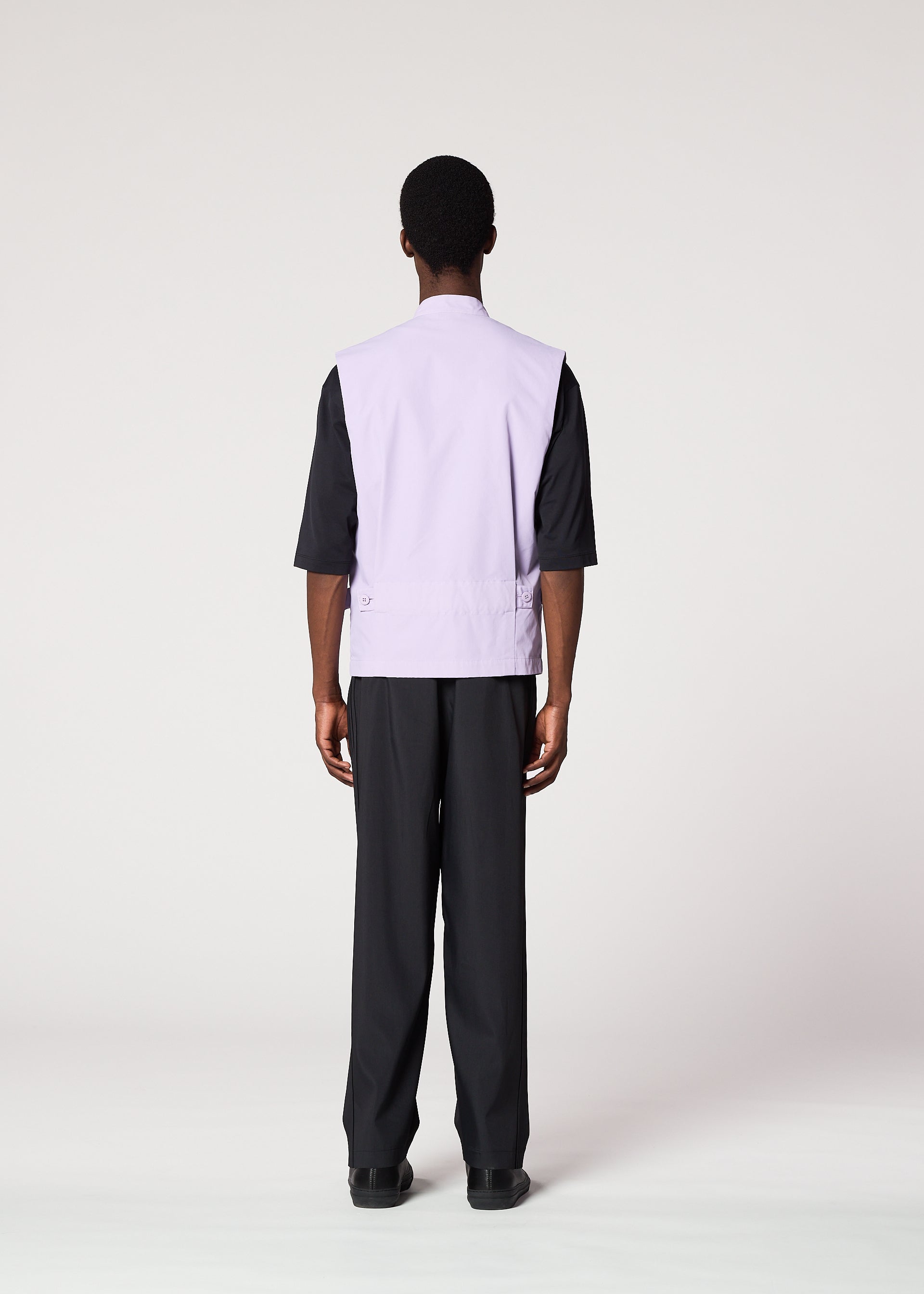 Zoomed view A person faces away from the camera, wearing IM MEN’s RESILIENCE—an airy light purple vest over a black elbow-sleeve shirt and black pants—ideal for everyday style, set against a plain light background.