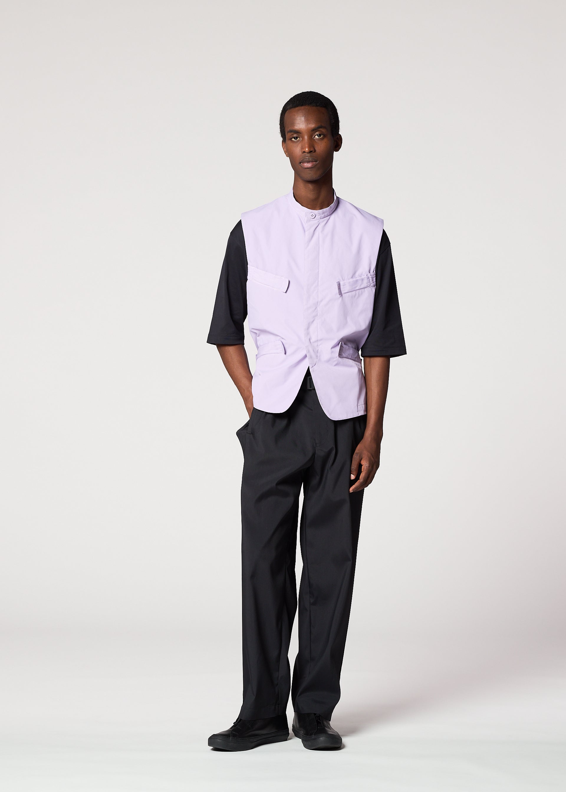 Zoomed view A man models the IM MEN RESILIENCE light purple, wrinkle-resistant vest over a black half-sleeve shirt and loose black pants, with his left hand in his pocket. The plain white background highlights this versatile everyday look.