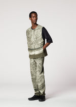 A man stands with hands in his vest pockets, wearing the KAIYU textured light-green ceramic artist vest and matching pants by IM MEN over a black shirt and black shoes, set against a plain light background.