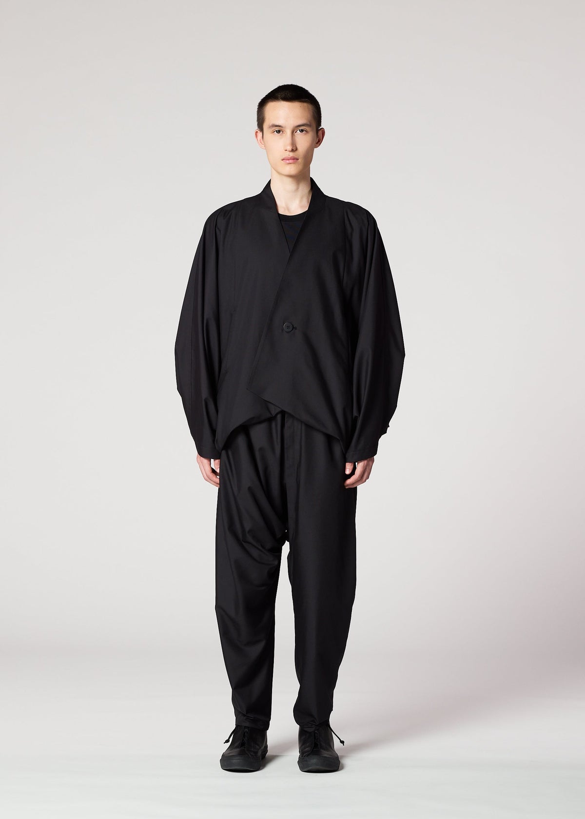 A person stands facing forward against a plain light background, wearing IM MEN's SWING BLACK loose-fitting jacket and wrinkle-resistant pants, both with a relaxed silhouette. Their expression is neutral and their arms rest at their sides. view 5 of 7