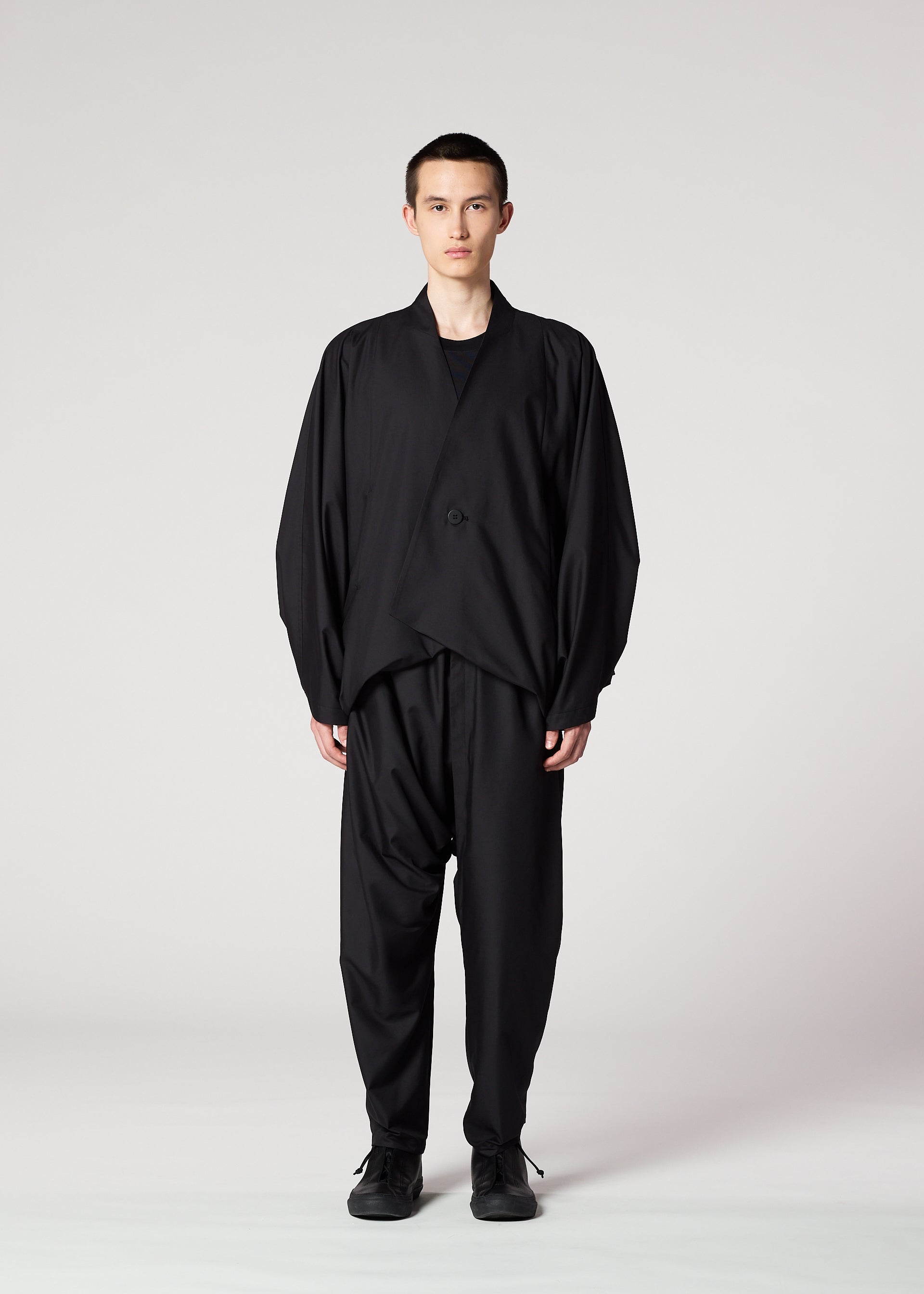 Zoomed view A person stands facing forward against a plain light background, wearing IM MEN's SWING BLACK loose-fitting jacket and wrinkle-resistant pants, both with a relaxed silhouette. Their expression is neutral and their arms rest at their sides.